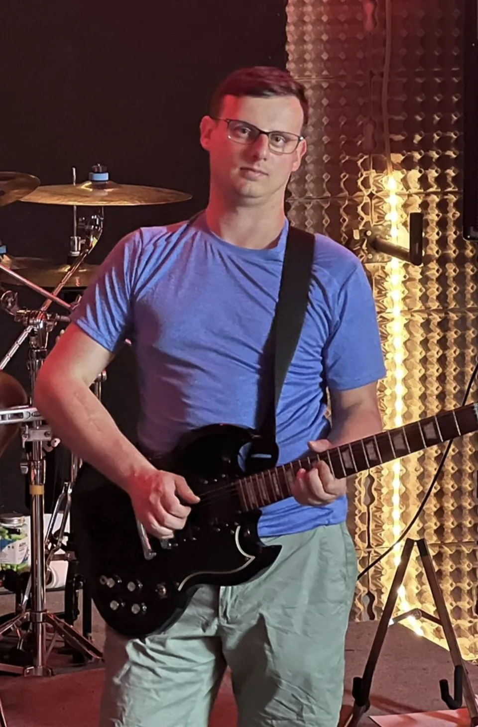 Adam z czarną gitarą elektryczną przy perkusji