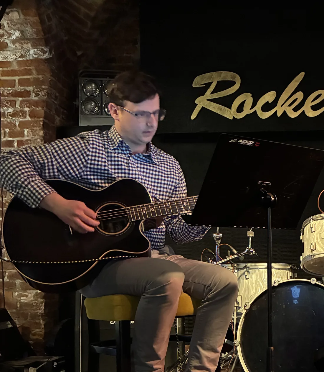 Adam z gitarą akustyczną na scenie w Rockerze