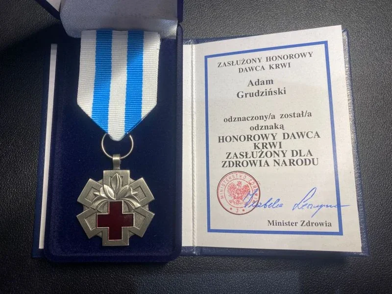 Odznaka Honorowy Dawca Krwi Zasłużony dla Zdrowia Narodu w etui, obok legitymacja z podpisem Ministra Zdrowia