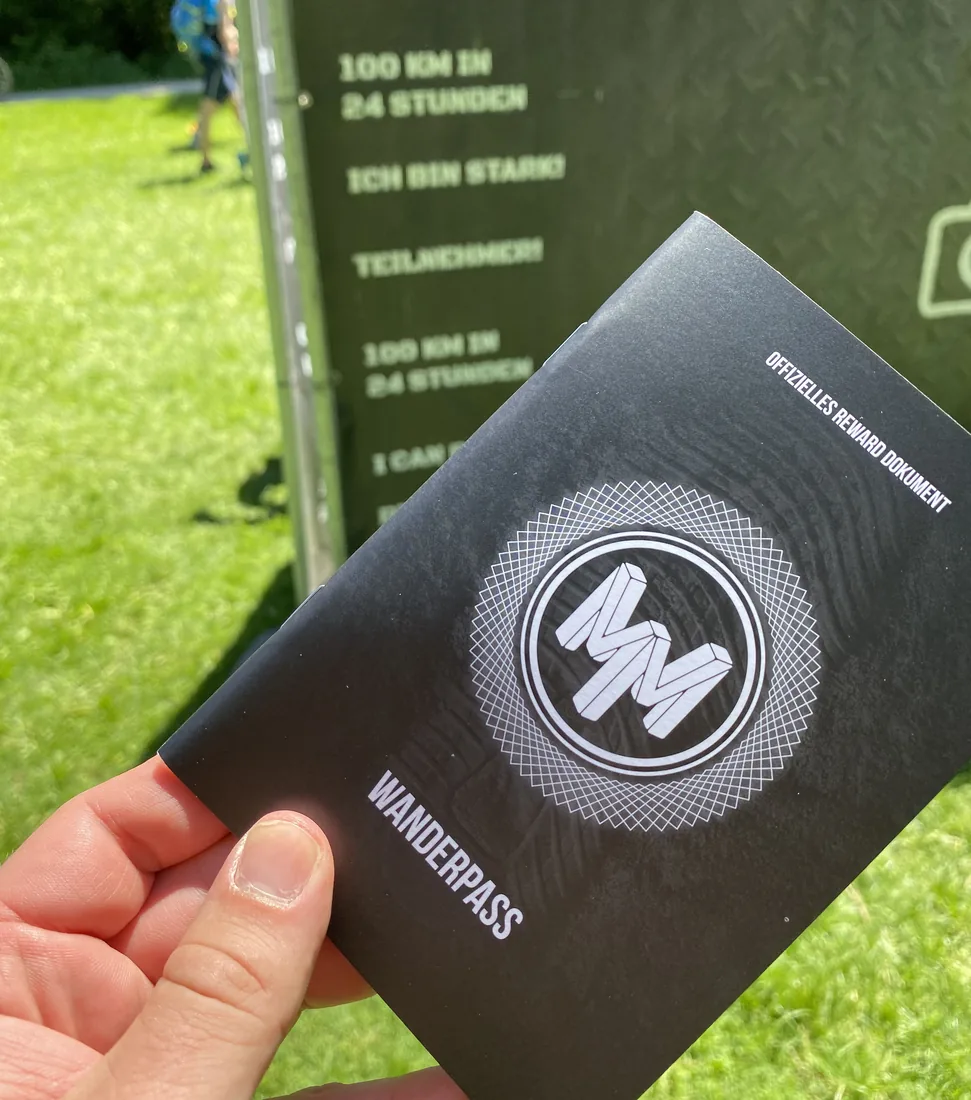 Wanderpass Mega Marsch w dłoni, w tle baner 100 km w 24 godziny