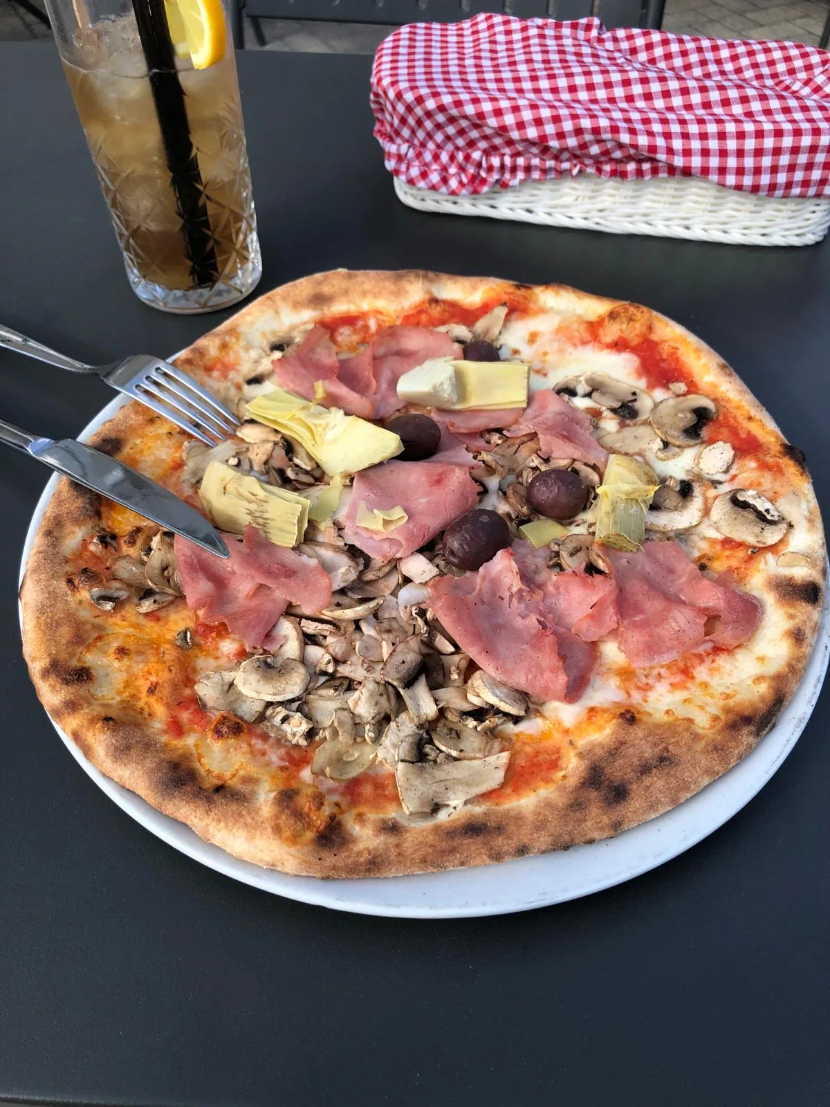 Pizza z szynką, karczochami i pieczarkami na stoliku